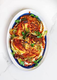 Golden seared cabbage wedges drizzled with spiced tomato butter, nestled on creamy yogurt, topped with fresh herbs.