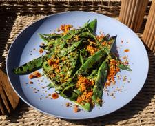 Charred runner beans with buttery gochujang pangrattato and sesame seeds on a blue plate, served outdoors in natural sunlight.